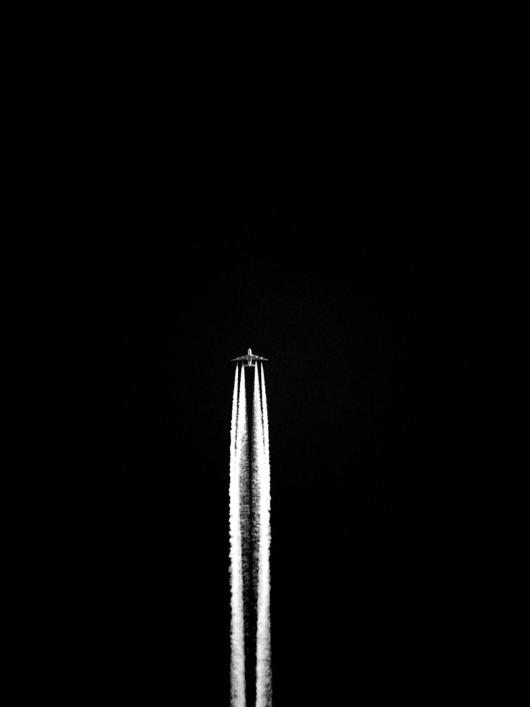 Ein Flugzeug mit 2 weißen Kondensstreifen vor einem schwarzen Hintergrund.